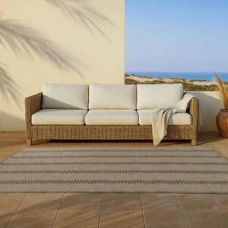 Tapete Zipper bege com padrão geométrico à frente de sofá de rattan num terraço junto ao mar