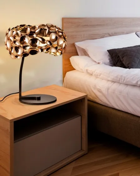 Candeeiro de mesa Narisa dourado com abajur escultural em criado-mudo ao lado da cama