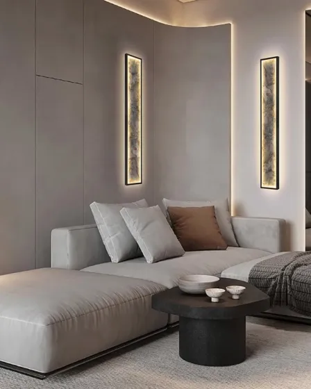 Aplique Stone L100 vertical iluminado numa sala moderna com sofá cinzento