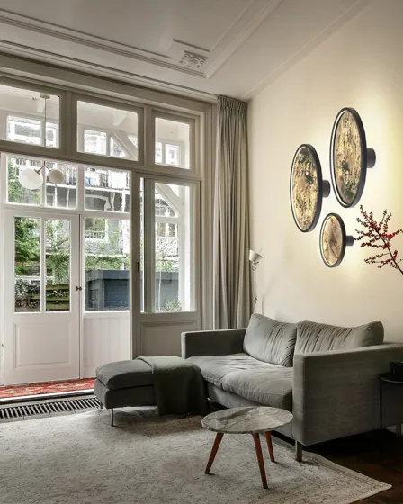 Aplique Stone D60 com três discos murais iluminados dourados acima de sofá cinzento