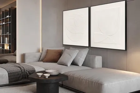 Set de quadros albos com relevo abstrato branco sobre sofá cinzento numa sala moderna