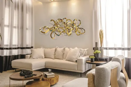 Escultura de parede Medusa dourada e abstrata acima de sofá numa sala luminosa