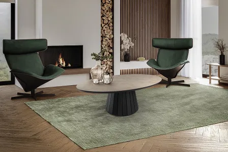 Mesa de centro Koria redonda com tampo claro e base preta canelada, sobre tapete verde