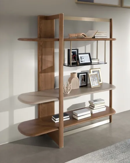 Livreiro Vidal em madeira com prateleiras arredondadas, livros e molduras decorativas