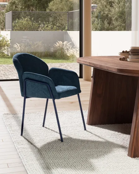 Cadeira Aslin azul escuro estofada com braços e pernas metálicas junto a mesa