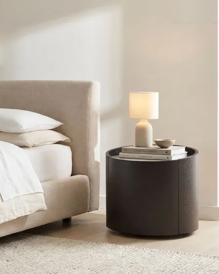 Mesa de cabeceira Iza redonda preta com candeeiro e livros ao lado da cama