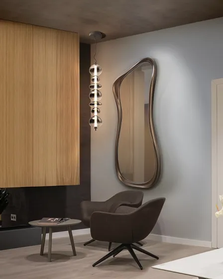 Espelho Gina de parede com moldura ondulada sobre poltrona e mesa lateral