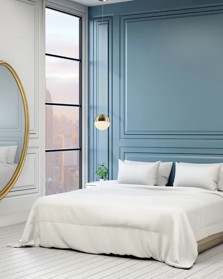 Espelho Brigitte oval dourado encostado na parede num quarto com cama branca