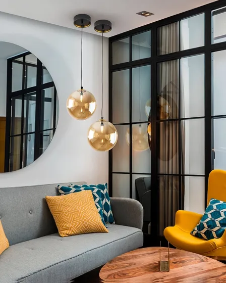 Candeeiro suspenso dark com dois globos dourados sobre sofá cinzento e mesa de madeira