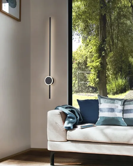 Aplique online vertical minimalista com anel luminoso junto a sofá e janela