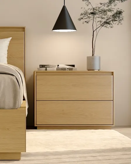 Mesa de cabeceira nórdica em madeira clara com duas gavetas, candeeiro e vaso.