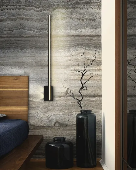 Aplique stick vertical minimalista em parede de pedra junto à cama e vasos negros