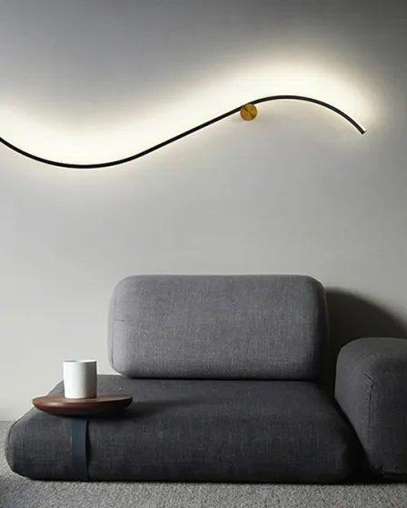 Aplique Siloe ondulado preto com detalhe dourado na parede acima de sofá cinzento