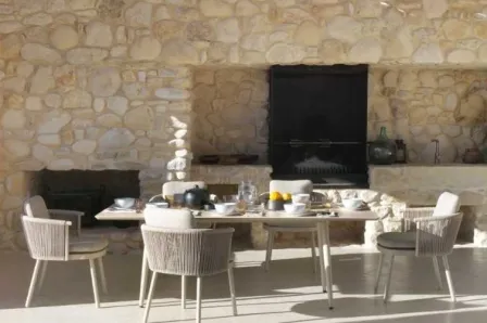 Mesa de jardim sabbia com quatro cadeiras e loiça numa esplanada junto a parede de pedra