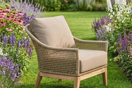 Poltrona de jardim Atesso em rattan sintético com almofada bege em relvado florido