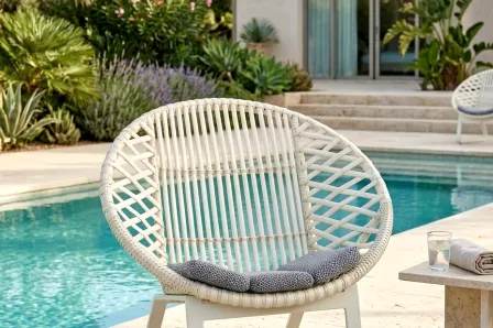 Poltrona de jardim circular branca com almofada cinzenta junto à piscina