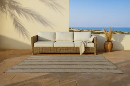 Tapete Zipper bege com padrão geométrico à frente de sofá de rattan num terraço junto ao mar